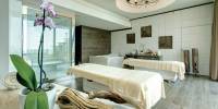 Rustic treatment room with twin massage beds, wooden flooring and furniture, ornamental drift wood and a potted orchid
