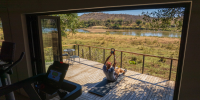 Man works out on a wooden deck with views of the African greenery and river