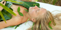 Woman lies with her blond hair spread out on a white bed covered in bamboo leaves
