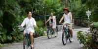 Cycling at Palmaïa – The House of AïA Two women and a man riding bikes on a path surrounded by tropical greenery