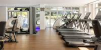 Gym with white walls, wooden floors and ceiling spotlights, with treadmills, weight machines and other equipment 