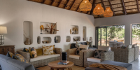 Lounge with a wood-beamed ceiling, rattan lantern lights, neutral sofas and shelves stacked with artisan decorations