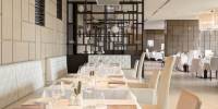 Airy restaurant with glossy tiled walls, dark-wood shelves stacked with ornaments, and white tablecloths