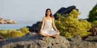 Woman sitting by the ocean practising meditation on rocks