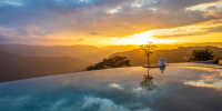 Infinity-edge pool at sunset, with mountains in the distance and a guest meditating on the edge