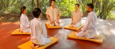 A group meditation in the open shala where guest sit on yellow cushions with their eyes closed 