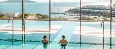 Couple relax in an indoor pool which leads outdoors and has views over the sea and islands