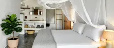 Bohemian-style bedroom with white bedding and a sheer white canopy, a potted plant and grey flooring