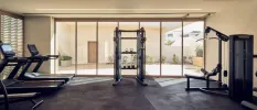 Gym with grey flooring and floor-to-ceiling windows overlooking a courtyard, with treadmills, weights machines and a bench