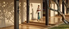 Staff member in traditional Sri Lankan dress walking through an open-air corridor with a tray of tea