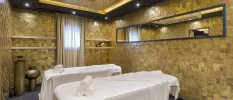 Treatment room with a gold chandelier and decorative pots, tiled walls and two massage beds covered in white towels