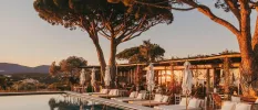 Swimming pool fringed with trees and views of the distant hills, surrounded by chic striped daybeds and white umbrellas