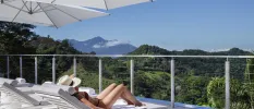 Woman sunbathing in swimwear and a hat on a lounger, overlooking green mountain peaks