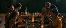 Group sit around a candlelit wooden table enjoying a meal at night-time