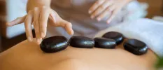 Therapist places black stones on the back of a guest lying on their front in a towel