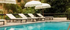Swimming pool lined with white-cushioned loungers and boho-style white umbrellas with fringing