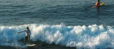 Man and woman on surf boards, one standing one paddling, in the ocean
