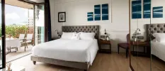 Modern hotel room with glass-door wardrobes, white bedding, a grey padded headboard and patio doors open to a furnished terrace