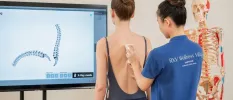 A therapist scans a woman's spine as she looks on at a screen showing it