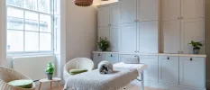 White treatment room with a bed, cupboards and a chair