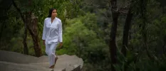 Woman in white strolls up a stone staircase surrounded by forest greenery