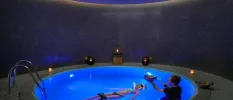 Woman relaxing on her back in a candelit pool as a therapist practices sound healing beside her