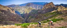Two people in active wear cycle in the mountains under a blue sky