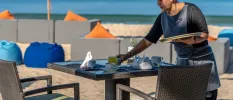 Staff member sets a table on the beachfront, with blue bean bags and orange cushions in the background