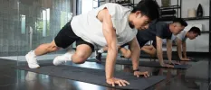 Three men in active wear in a plank position on yoga mats in an airy studio