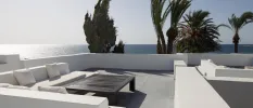 A sleek paved terrace with a white sofa and dark-wood coffee table overlooking the sea and palm trees
