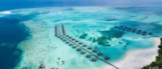 Over-water villas in turquoise shallows in the Maldives, overlooking a white-sand beach and an island with a lush interior