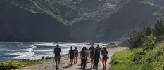 Group of people hiking next to water and surrounded by green mountains 