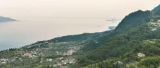 Aerial view of green hills and a village below on the edge of Lake Garda