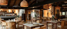 Rustic, boho-style restaurant with rattan lantern ceiling lights, wooden tables and chairs, wood-beamed ceilings and a Buddha statue 