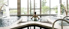 Woman in a white swimsuit relaxes in an indoor pool with floor-to-ceiling windows