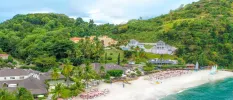 Sprawling grey-roofed resort among lush greenery overlooking a white-sand beach