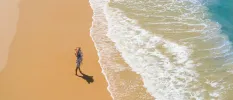 Woman in a straw hat and floral dress stands on the shoreline 