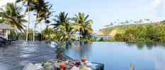 Infinity pool overlooking the sea and tropical gardens with a table next to it laid up with fruit, salads and smoothies