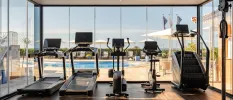 Treadmills, bikes and a stepper in a gym with floor-to-ceiling windows overlooking a pool
