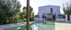 White cube-shaped villa with a rectangular pool, cobbled stone terrace and surrounding greenery