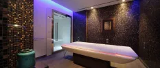Tiled spa treatment room with mood lighting in blue, and a massage bed draped in a white fabric