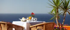Table with a white tablecloth laid on a sunny terrace overlooking palm trees and the sea