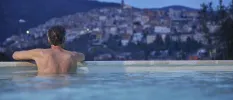Man in a swimming pool looks out towards the hillside town of Fiuggi as the sky darkens