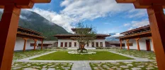 Monastery courtyard with a tree at the centre and green hills in the background under a cloudy blue sky