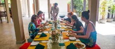 Group of women sitting around a colourful table eating as a staff member pours a drink at the end
