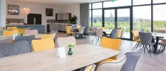 Wooden tables with grey and yellow chairs and floor-to-ceiling windows