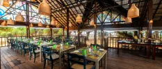 Airy dark-wood restaurant with open sides, rattan lantern-style pendant lights and tables with floral tiled tops