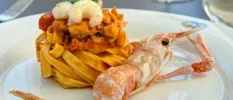 A mound of pasta on a white plate topped with prawns with a prawn that hasn't been shelled to one side