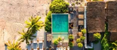 Swimming pool, thatched-roof buildings, loungers and a sandy beach covered in tropical greenery, as seen from above