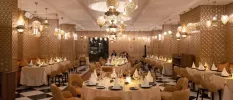 Lantern-lit restaurant with intricately patterned pillars, a black and white chequered floor and tables with gold chairs and beige tablecloths
